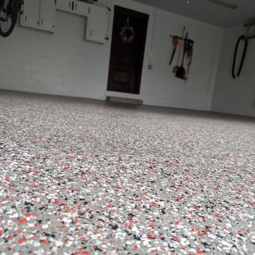 This image shows a garage interior with speckled epoxy flooring. White cabinets and organized tools are visible against the white walls, with a door in the background.