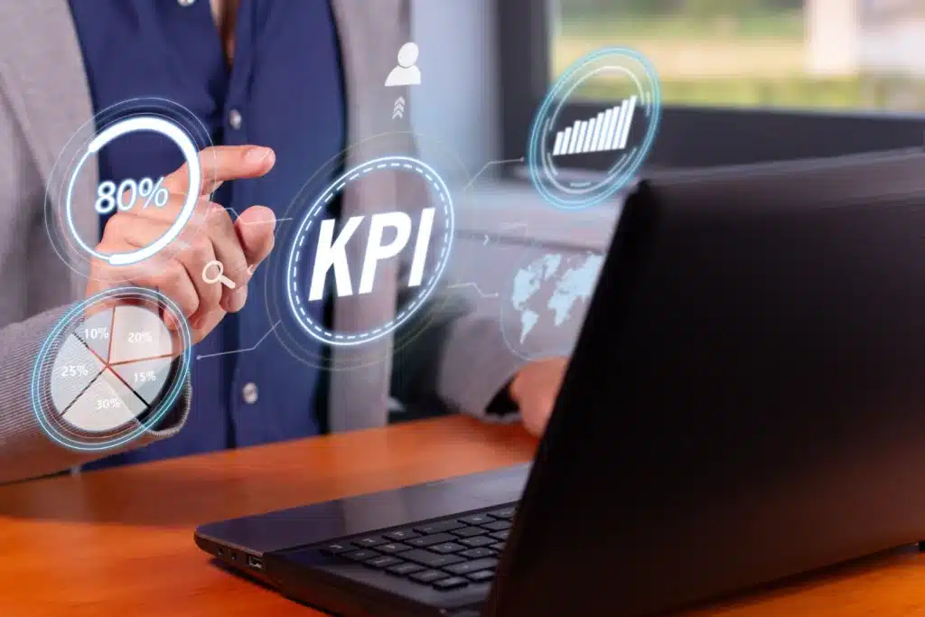 A person interacts with a futuristic interface showing KPI and data graphics above a laptop, symbolizing modern business analytics and management.